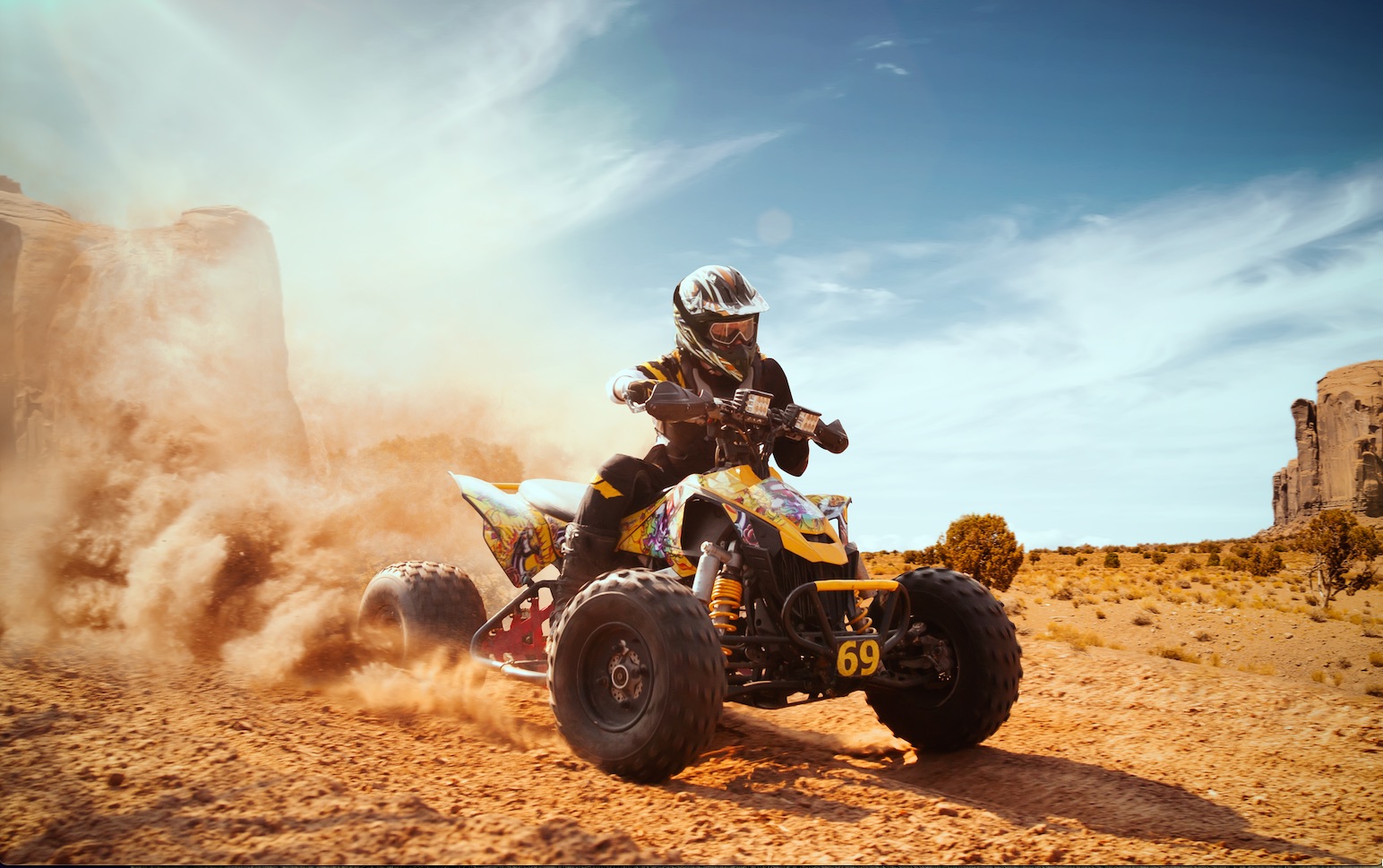 helmeted rider driving an ATV through dirt kicking up a cloud of dust